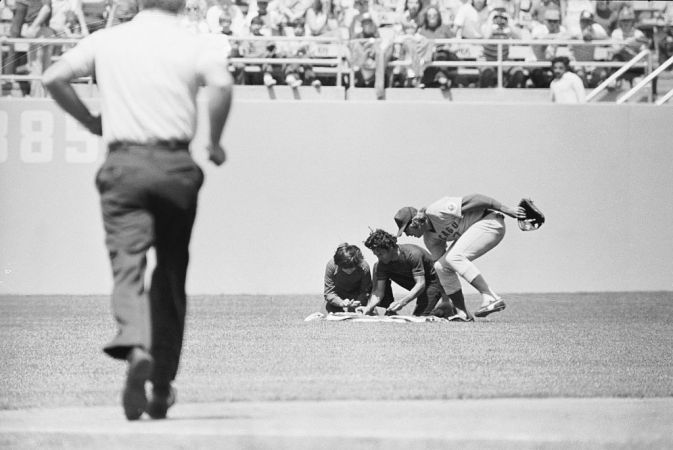 (Original Caption) April 25, 1976-Los Angeles, California: On a dead run from centerfield, Chicago Cubs Rick Monday reaches to rescue an American flag as two men attempt to set the flag on fire during 4th inning play in Dodgers Stadium. First reports said the men, a father and son, were protesting treatment of American Indians. The flag was wet with lighter fluid but the men were unable to light their matches.