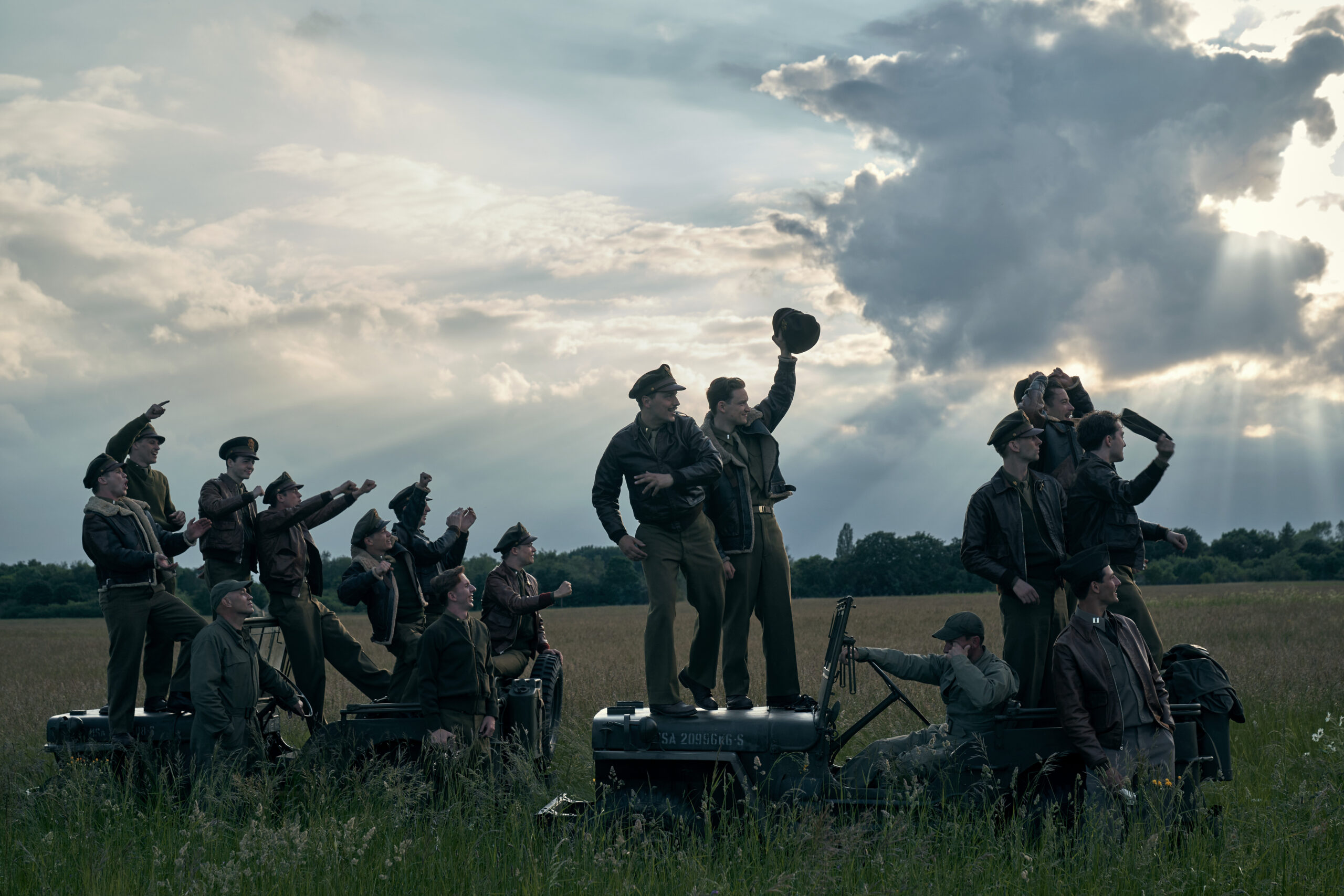 Men from Masters of the Air cheering in a field.