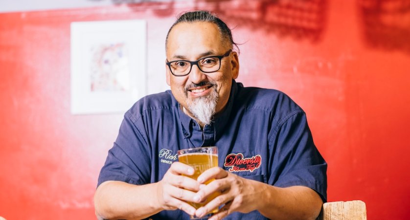 Richard Fierro standing in front of a red wall and holding a beer.