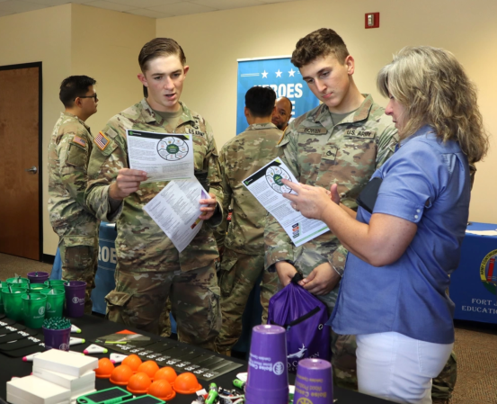 Two uniformed service members look at papers with a woman