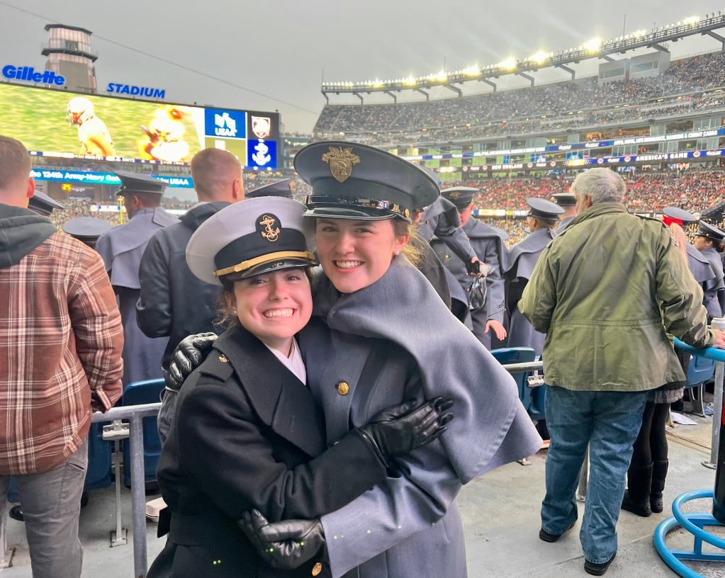 A Naval Academy midshipman and West Point cadet hug in the Gillette stadium