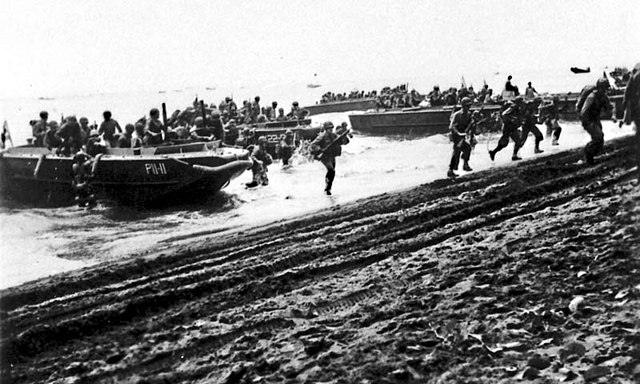 U.S. First Division Marines storm ashore across Guadalcanal's beaches on D-Day, 7 August 1942, from the attack transport USS Barnett (AP-11) and the attack cargo ship USS Fomalhaut (AK-22).