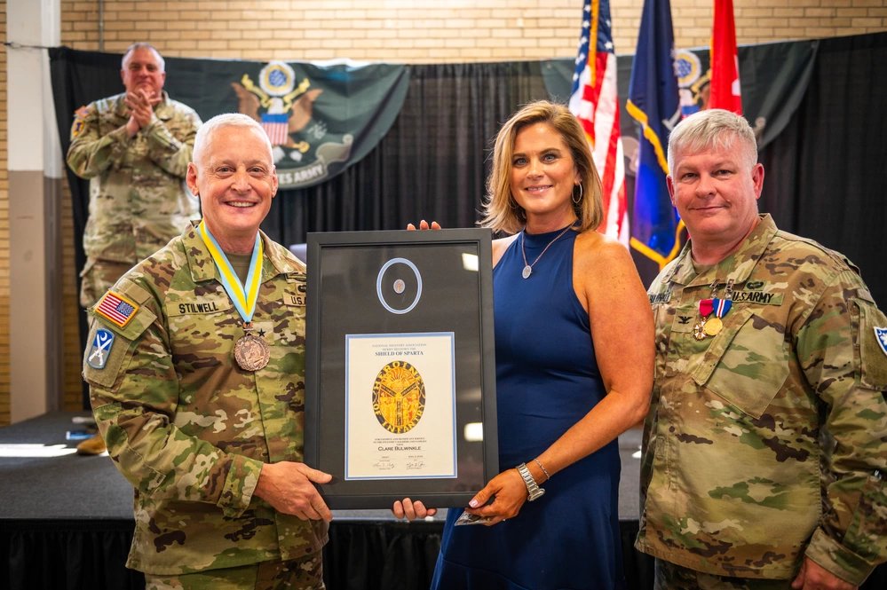 U.S. Army Brig. Gen. Robin Stilwell, director of the joint staff (left), awards Clare Bulwinkle (center), the Shield of Sparta and a certificate of aprecation, Aug. 9, 2024 in Columbia, South Carolina. The Shield of Sparta is to those who contributed significantly to the infantry and is a token of appreciation for the sacrifice and commitment demanded of the spouses and supporters of infantrymen and other soldiers. (U.S. Army National Guard photo by Staff Sgt. Tim Andrews)