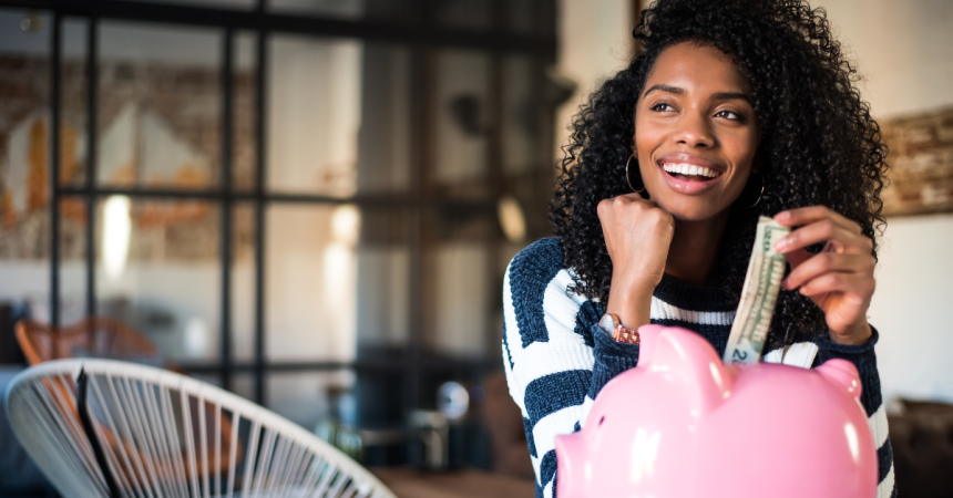 A young Black woman deposits money into a piggy bank