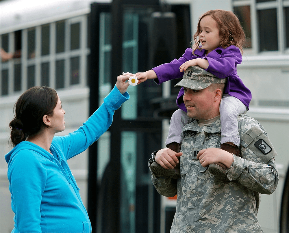 A little girl sits on her dad's shoulders and hands her mom a flower