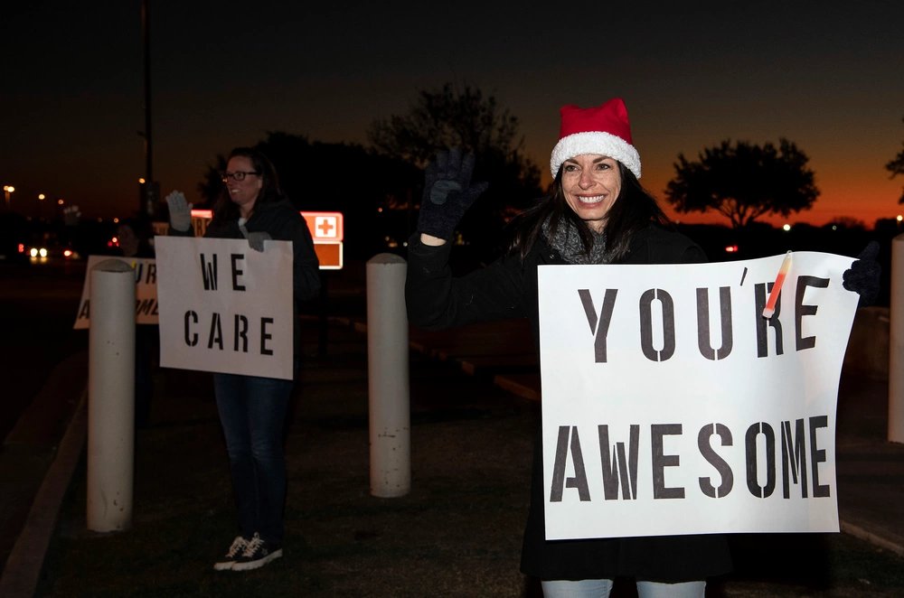 Leslie Janaros, 37th Training Wing key spouse mentor and wife of Col. Jason Janaros, 37th TRW commander, holds a positive message of support at a base gate during the morning inbound commute as part of their new initiative, “We Care,” at Joint Base San Antonio-Lackland, Texas, Dec. 18, 2019. The 323rd Training Squadron started the initiative which involved 37th Training Wing military and civilian members spending the morning at various gates letting each person know that they stand together in support of those struggling with depression and thoughts of suicide by holding a positive message of support and handing out over 400 candy canes. If you are struggling with thoughts of suicide, please go directly to the Mental Health Clinic or to your closest Emergency Room. You can also reach the National Suicide Prevention Lifeline at 1-800-273-8255.