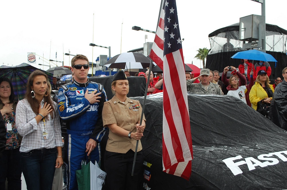 Aviation Ordnanceman 1st Class Noami Stout, assigned to Patrol Squadron (VP) 8, holds the American flag NASCAR driver Carl Edwards during the national anthem at the 54th running of the Daytona 500. Stouts rode a lap around the famed speedway with Edwards before the race.