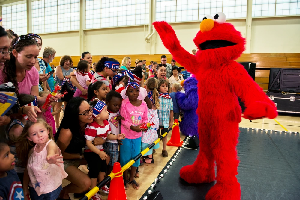 Sesame Street character Elmo waves to the audience at the completion of the Sesame Street USO Experience for Military Families show at Travis Air Force Base, Calif. The Sesame Street USO Experience for Military Families is a 35 minute show featuring four of the popular Sesame Street costumed characters, as well as Katie, a military child created especially for the USO. Katie appears in two shows, the “moving show” which depicts her leaving friends as she moves to a new base and the “transition show” in which her family is permanently separating from the military, June 6, 2016. (U.S. Air Force photo by Louis Briscese/Released)