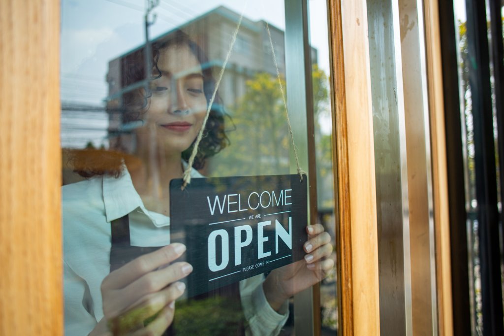 Store owner woman turning open sign wood broad to ready service food and beverage to customer.Asian entrepreneur leaning.Asian waiter stand and flip advertise hanging in front of coffee shop.